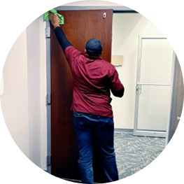 Cleaning staff member wiping the top of an office door in a corporate hallway